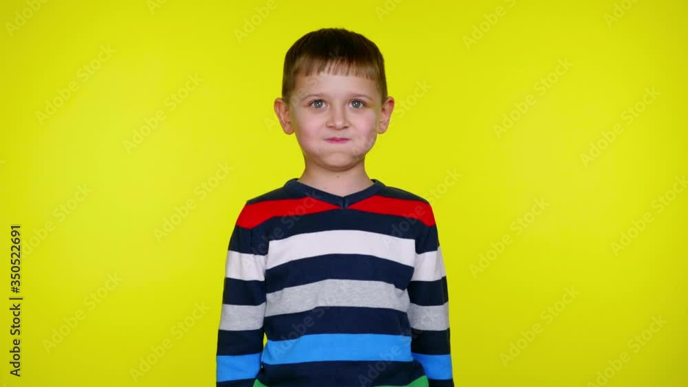 Confused little child boy in a colorful sweater on a yellow background with copy space. Place for text or product. 4K slowmotion footage Confused little child boy in a colorful sweater on a yellow background with copy space. Place for text or product. 4K slowmotion footage