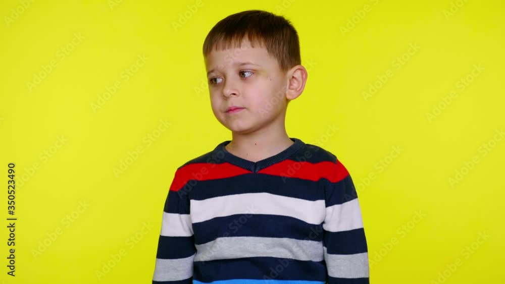 Confused little child boy in a colorful sweater looks to the right and thinks on yellow background with copy space. Place for text or product. 4K slowmotion footage Confused little child boy in a colorful sweater looks to the right and thinks on yellow background with copy space. Place for text or product. 4K slowmotion footage