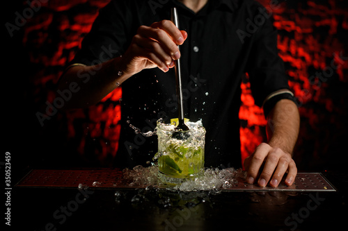 professional barman making alcoholic cocktail in glass which splashing out