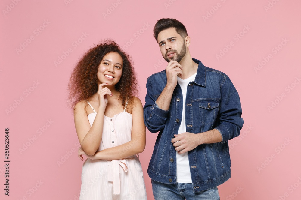 Pensive couple two friends european guy african american girl in casual clothes isolated on pastel pink background. People lifestyle concept. Mock up copy space. Put hands prop up on chin, looking up. Pensive couple two friends european guy african american girl in casual clothes isolated on pastel pink background. People lifestyle concept. Mock up copy space. Put hands prop up on chin, looking up.