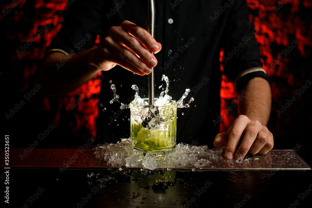 Male bartender making alcoholic cocktail in glass which splashing out