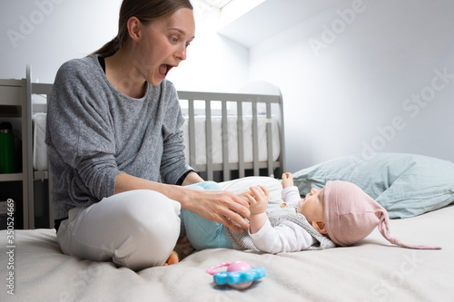 Foto Happy funny mom grimacing and playing with baby daughter in bed