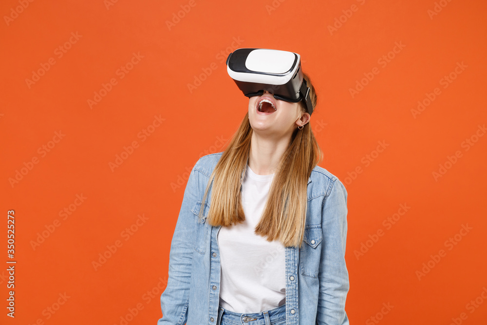 Fototapeta premium Excited young woman girl in casual denim clothes posing isolated on bright orange wall background studio portrait. People sincere emotions lifestyle concept. Mock up copy space. Watching in headset.