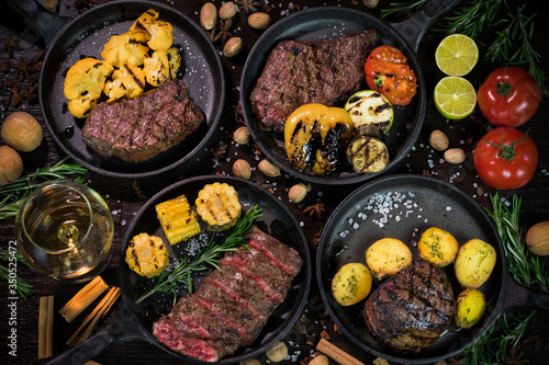 different types of grilled steaks, decorated with tomatoes, walnuts and cinnamon on a dark background