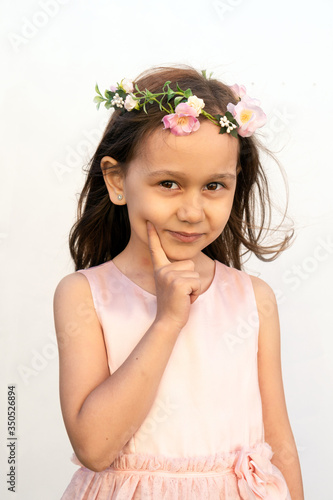 Portrait of a girl of 7 years old with brown hair and brown eyes in a gently peach dress with a wreath of flowers on her head on a white background. Spring girl. Summer time