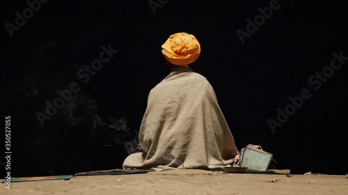 Portrait of sadhu or holy man praying and meditating on Ghats of Varanasi in front of the sacred river Ganges, India, dark time