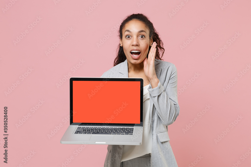 Excited african american business woman in grey suit white shirt isolated on pink background. Achievement career wealth business concept. Hold laptop pc computer with blank screen, put hand on cheek. Excited african american business woman in grey suit white shirt isolated on pink background. Achievement career wealth business concept. Hold laptop pc computer with blank screen, put hand on cheek.