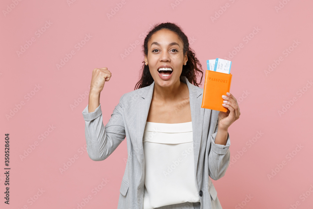 Joyful young african american business woman in grey suit white shirt isolated on pink background. Achievement career wealth business concept. Hold passport tickets boarding pass doing winner gesture. Joyful young african american business woman in grey suit white shirt isolated on pink background. Achievement career wealth business concept. Hold passport tickets boarding pass doing winner gesture.