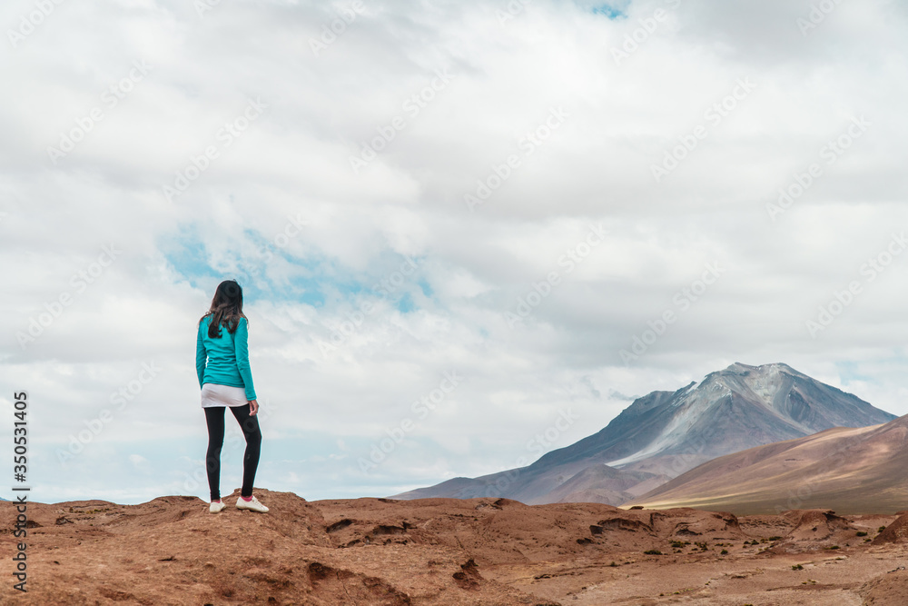 Tourist woman hiking Rocky landscape mountain. Dry, Barren desert, snowcapped mountains wilderness. Mountain range view. Salt Flats, Uyuni, Bolivia. Copy space, Rocks, blue sky, nature, hiker