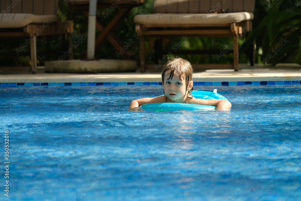 Kids having fun with Inflatable circle in the swimming pool with clear blue water. Summertime, vacation concept.