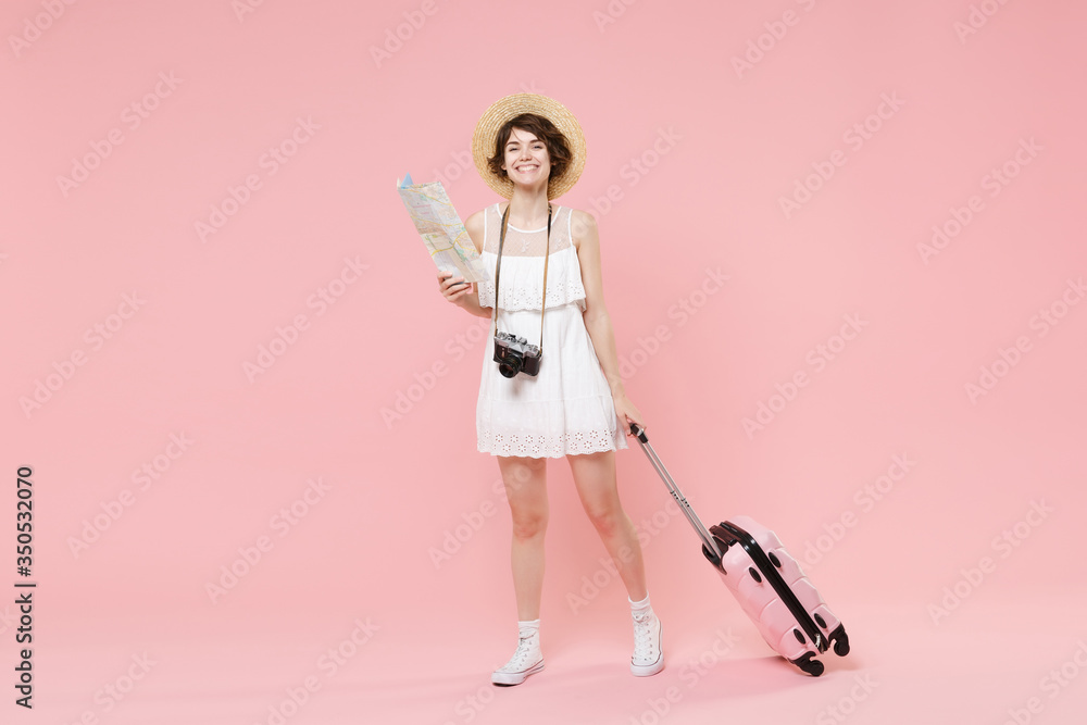 Smiling tourist girl in summer white dress hat with suitcase photo camera isolated on pink background. Female traveling abroad to travel weekends getaway. Air flight journey concept. Hold city map. Smiling tourist girl in summer white dress hat with suitcase photo camera isolated on pink background. Female traveling abroad to travel weekends getaway. Air flight journey concept. Hold city map.