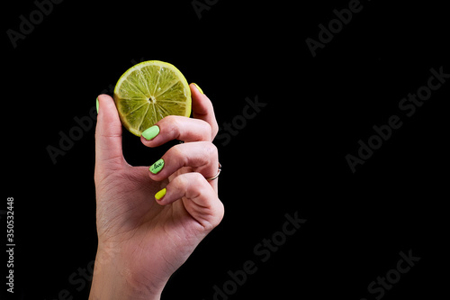 Fresh green lime in a female hand on a black background.