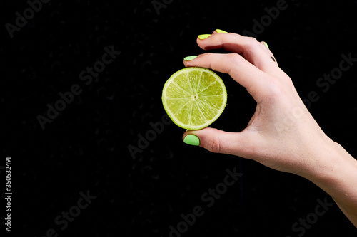 Fresh green lime in a female hand on a black background.