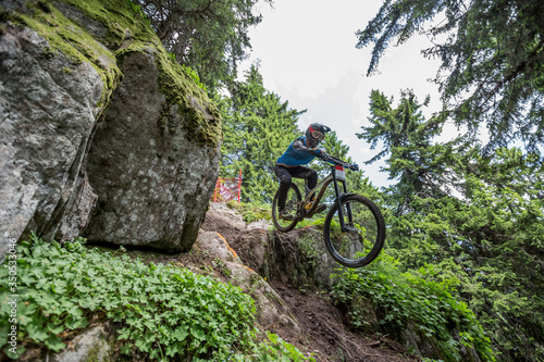 Man on mountain bike rides on trails trough the forest and jumps off cliff. 
