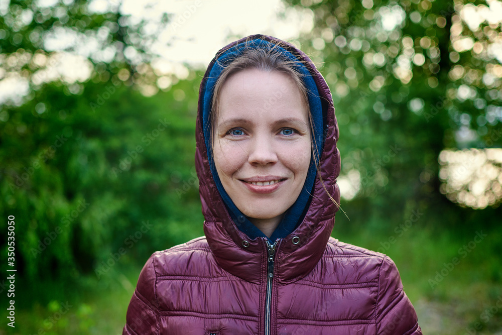 A middle aged woman in a jacket in a park is smiling. A middle aged woman in a jacket in a park is smiling.
