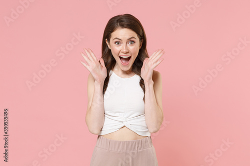 Excited young brunette woman girl in light casual clothes posing isolated on pastel pink background studio portrait. People lifestyle concept. Mock up copy space. Keeping mouth open, spreading hands.