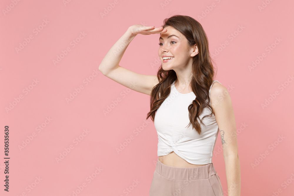 Smiling young brunette woman girl in light casual clothes posing isolated on pastel pink background. People lifestyle concept. Mock up copy space. Holding hand at forehead looking far away distance. Smiling young brunette woman girl in light casual clothes posing isolated on pastel pink background. People lifestyle concept. Mock up copy space. Holding hand at forehead looking far away distance.