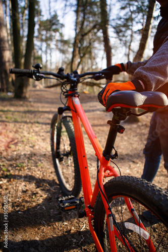 Bicycle with orange frame in the forest on the highway. A bicyclist in black and orange gloves holds the bike by the frame and seat. Theme of Cycling, sports, healthy lifestyle