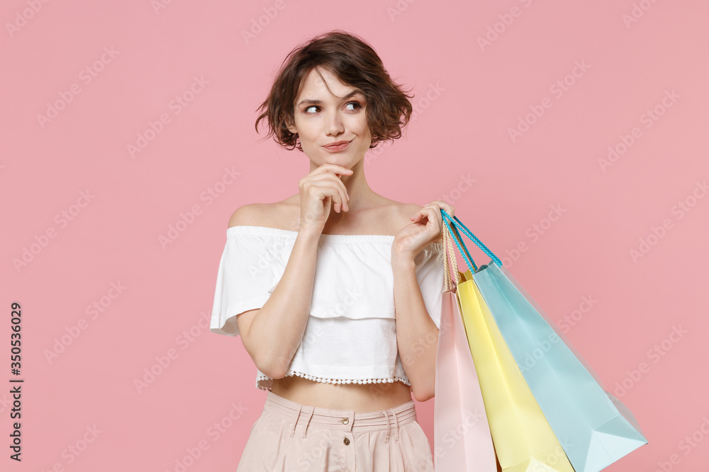 Pensive young woman girl in summer clothes hold package bag with purchases isolated on pink background studio portrait. Shopping discount sale concept. Mock up copy space. Put hand prop up on chin. Pensive young woman girl in summer clothes hold package bag with purchases isolated on pink background studio portrait. Shopping discount sale concept. Mock up copy space. Put hand prop up on chin.