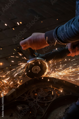 Side view of a man's hands working on a metal part of a garden bench, using an electric grinder while sparks are flying around in the industrial workshop © Dasya - Dasya