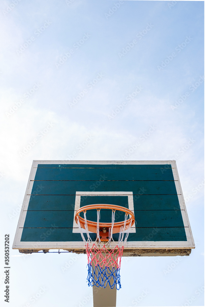 A perspective view of a dark basketball backboard with a multi-colored basketball basket against a bright sky. A perspective view of a dark basketball backboard with a multi-colored basketball basket against a bright sky.