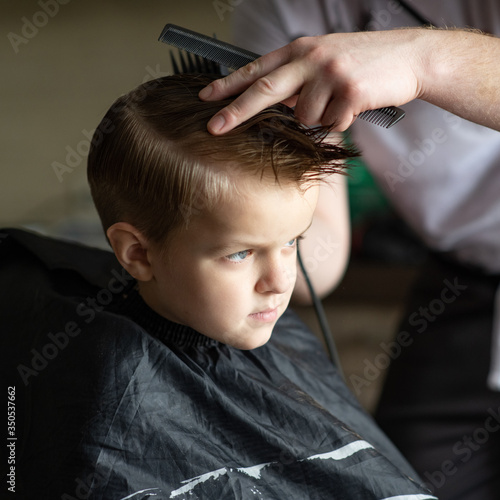Barbershop and hairdressing at home. Men's and children's haircuts. The hairdresser cuts the boy. Stylish hairstyle for a child