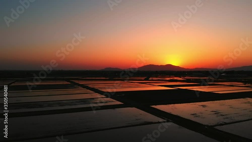 夕日が沈む山と春の田んぼに映り込むオレンジ