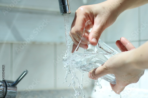 Wasser fließt aus dem Wasserhahn. Frau spült Gläser im Geschirrkorb. photo