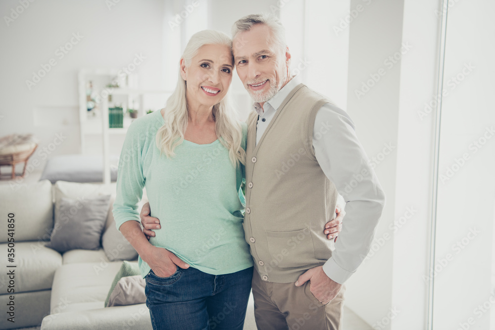 Portrairt of attractive grandparents cuddling looking dressed jeans denim trousers turquoise brown pullovers standing in big room Portrairt of attractive grandparents cuddling looking dressed jeans denim trousers turquoise brown pullovers standing in big room