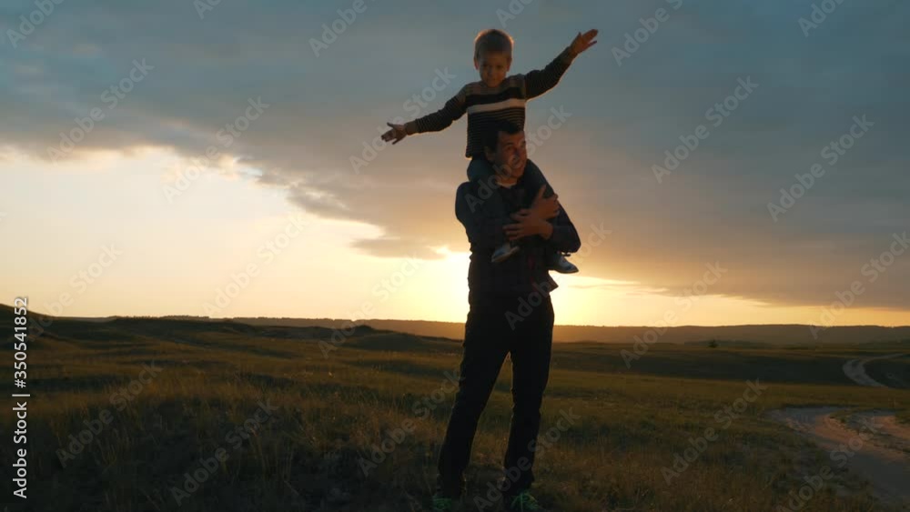 Silhouette of a happy family at sunset. The son sits on the shoulders of his father and depicts the flight of an airplane. The family is relaxing in the fresh air, dreaming of traveling. Silhouette of a happy family at sunset. The son sits on the shoulders of his father and depicts the flight of an airplane. The family is relaxing in the fresh air, dreaming of traveling.