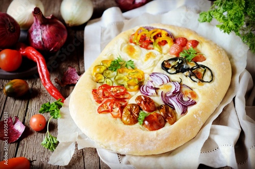 Homemade focaccia with different types of vegetables on a wooden background