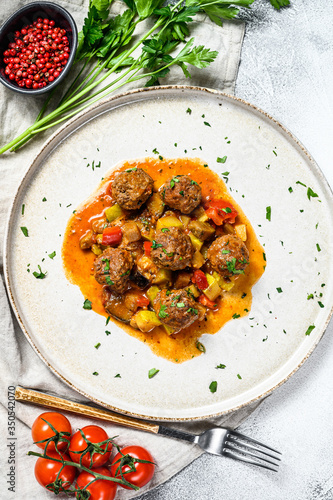 Pork meatballs with tomato sauce and vegetables in a pan. Gray background. Top view