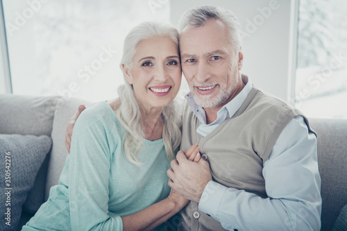 Photo of pretty aged pair leaning heads holding hands posing family portrait sitting cozy sofa indoors