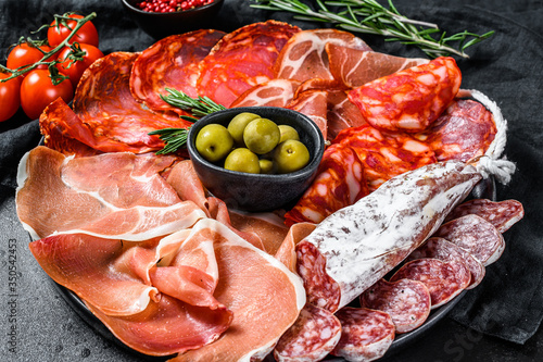 Cured meat platter of traditional Spanish tapas. Chorizo, jamon serrano, lomo and fuet. Black background. Top view.