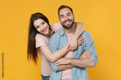 Cheerful laughing young couple two friends guy girl in pastel blue casual clothes isolated on yellow background in studio. People lifestyle concept. Mock up copy space. Hugging, holding hands crossed.