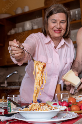 Signora anziana versa un abbondante porzione di spaghetti al pomodoro in un piato nella sua cucina photo