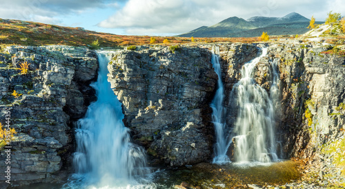 The bridal veil waterfall in Rondane national park in Norway during autumn. Colorful scenery and snow capped mountains in the background. photo