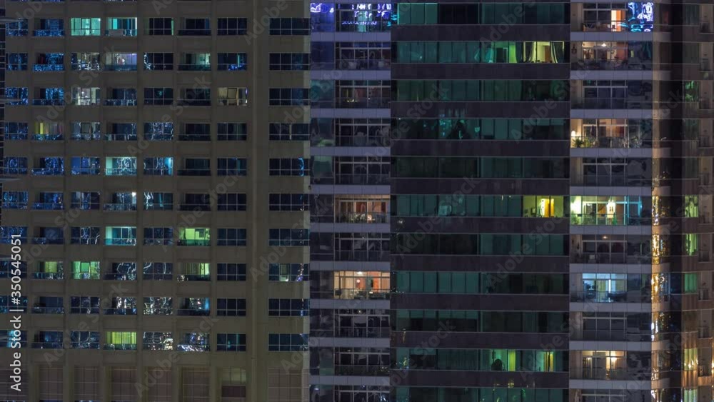 Rows of glowing windows with people in the interior of apartment buildings at night. Modern skyscrapers with glass surface. Concept for business and modern life Rows of glowing windows with people in the interior of apartment buildings at night. Modern skyscrapers with glass surface. Concept for business and modern life