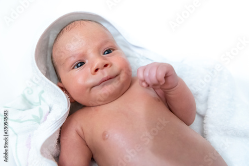 Adorable 2 months old little baby boy on towel after bath making funny face over white background