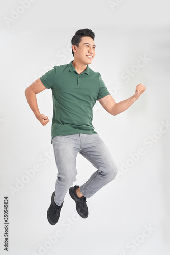 Image of cheerful young man dressed in green t-shirt jumping over white background make winner gesture.