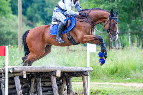 Eventing: equestrian rider jumping over an a log fence obstacle © Dotana