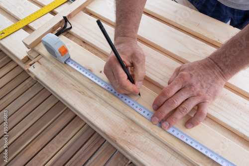 Man drawing line on wooden shelf and holding construction ruler. Carpenter working at balcony with wood. House improving, DIY and home decoration during quarantine concept