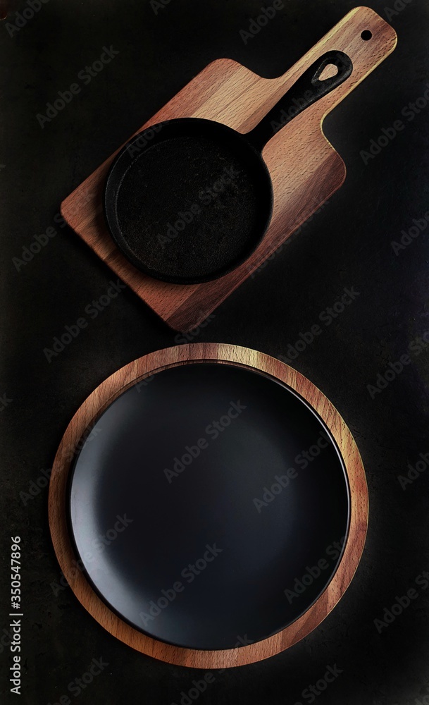 Black cutlery: a plate and a frying pan on a wooden stand