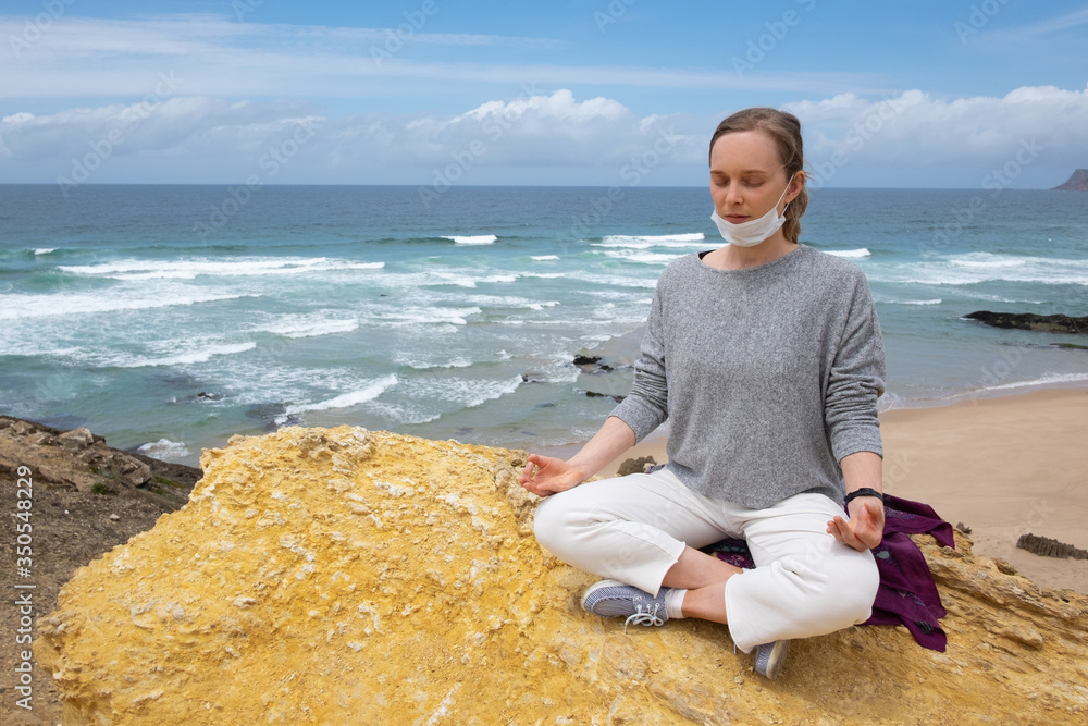 Tranquil woman in face mask practicing yoga and meditation outdoors, keeping arms in zen gesture. Copy space. Staying well during outbreak concept Tranquil woman in face mask practicing yoga and meditation outdoors, keeping arms in zen gesture. Copy space. Staying well during outbreak concept