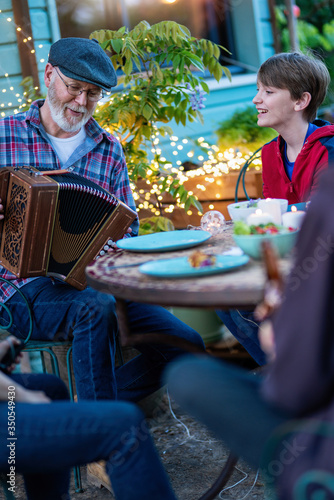 In the evening, dinner with friends around a table in the garden, in front of the wooden house. A bearded man plays the accordion for everyone's enjoyment. photo