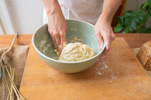 Cook kneading dough in bowl for delicious pastry and bread. Ceramic bowl standing on wooden board. Fresh cereal loaf. Studio shot. Side view. Homemade bakery and cooking at home concept