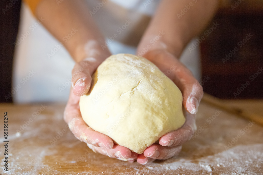 Unrecognizable baker holding kneaded dough in palms. Wheat flour on wooden board. Selective focus. Studio shot. Front view. Cooking and baking at home concept Unrecognizable baker holding kneaded dough in palms. Wheat flour on wooden board. Selective focus. Studio shot. Front view. Cooking and baking at home concept