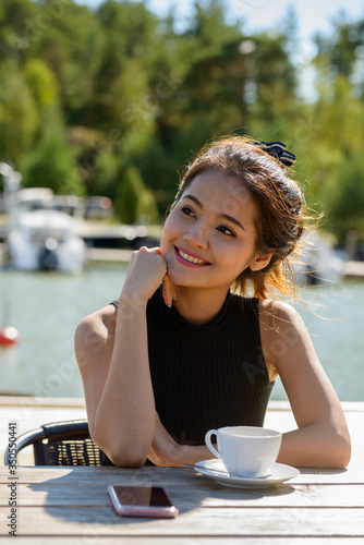 Happy young beautiful Asian tourist woman thinking at restaurant by the pier