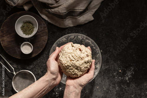 Girl holds kneading dough for homemade bread with herbs on a dark stone table. Cooking at home ourselves