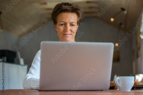 Happy mature beautiful woman with short hair using laptop inside coffee shop